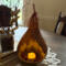 A rustic table centerpiece showing a natural gourd lit with a candle. It sits on a burlap cloth with a bouquet of twigs near.